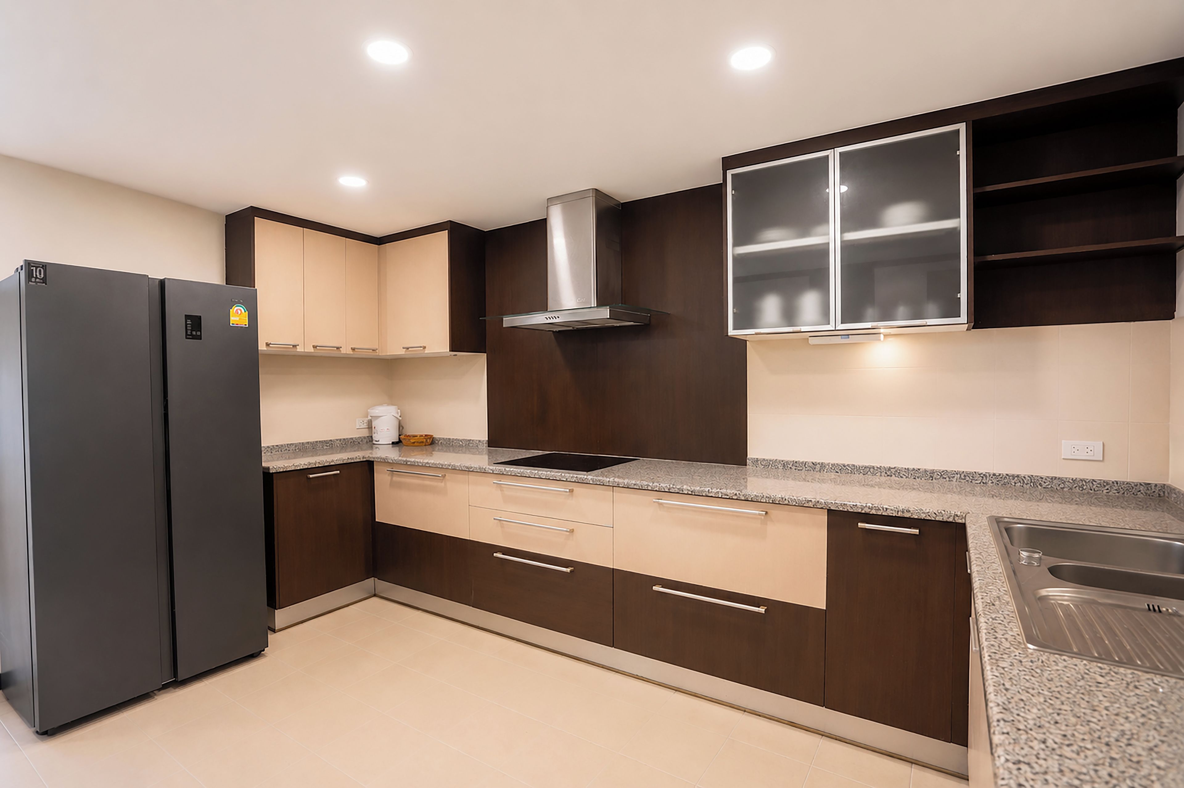 Una cocina moderna con armarios oscuros, un refrigerador de acero inoxidable, una estufa empotrada y un lavamanos doble.