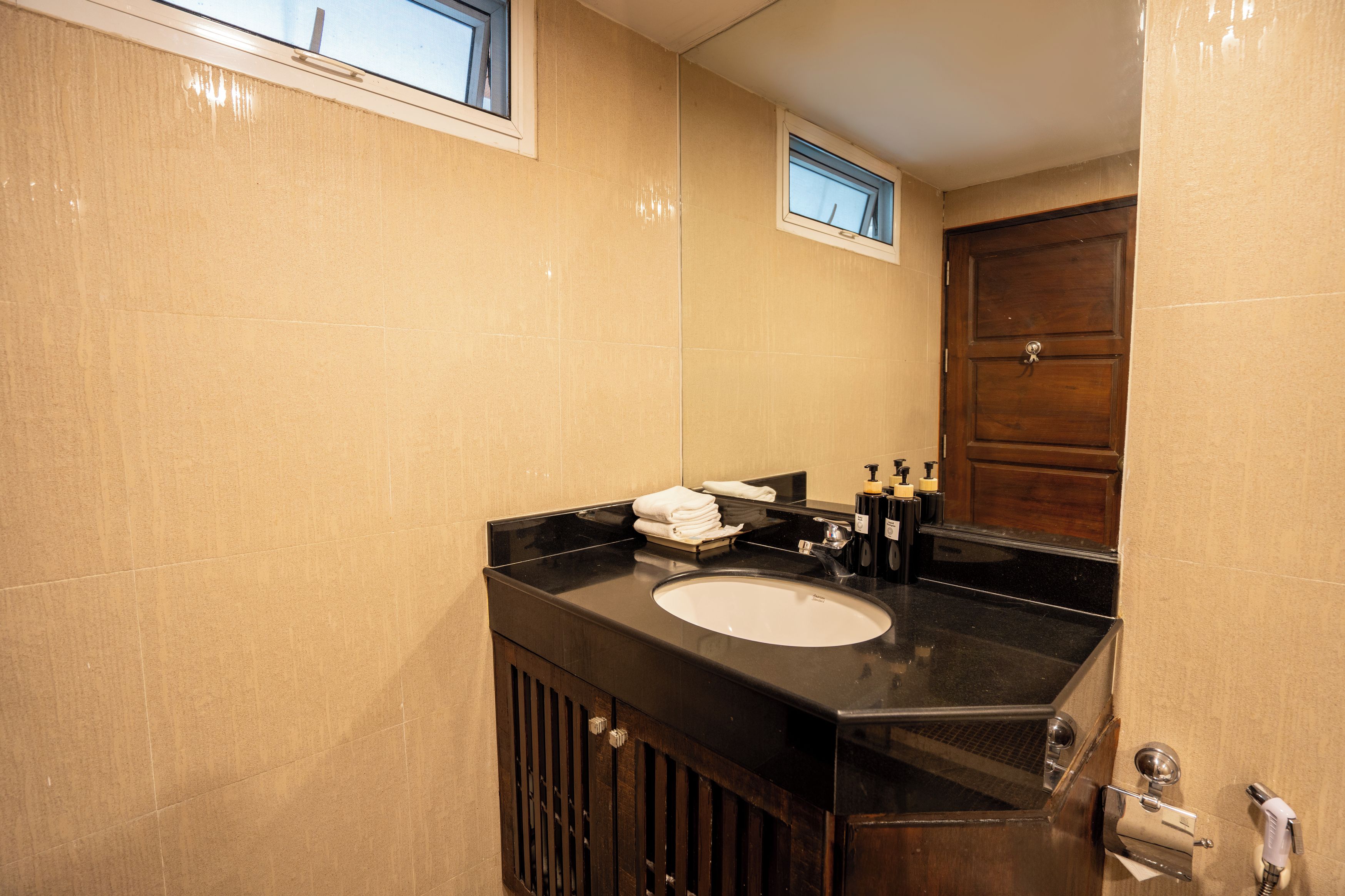 Un baño con encimera negra, lavamanos blanco y puerta de madera.
