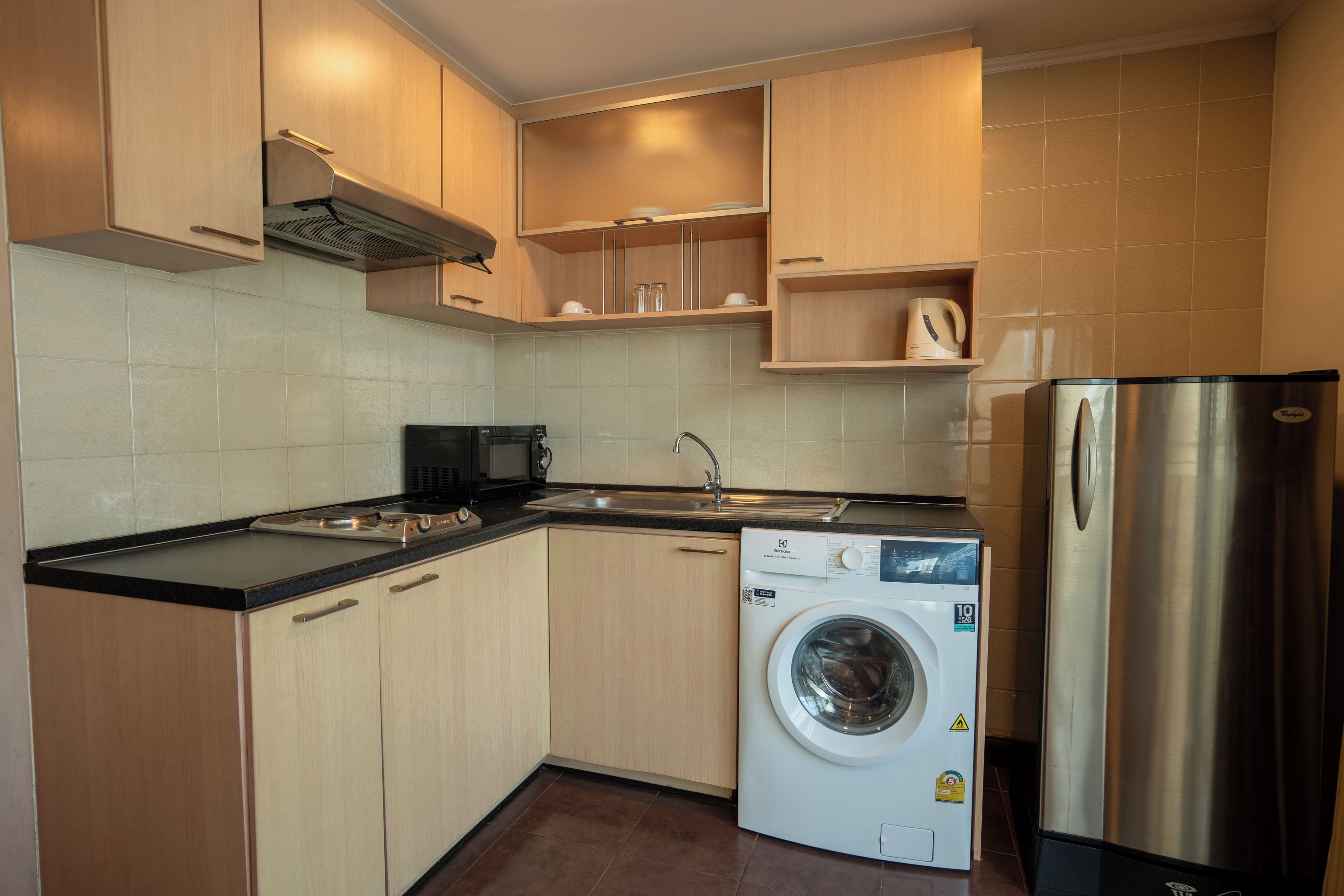 Eine moderne Küche mit Holzausbau, einem Edelstahlkühlschrank, einer integrierten Waschmaschine und einer Mikrowelle.