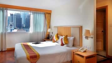 Habitación de hotel con una cama grande, una mesita de noche con lámpara, teléfono y vistas a edificios altos por la ventana.