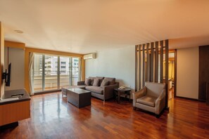 A modern living room with a sectional sofa, a small round table, and a chair. There is a large window with a view of buildings outside. - The Mercer Sukhumvit 4 (Bangkok)