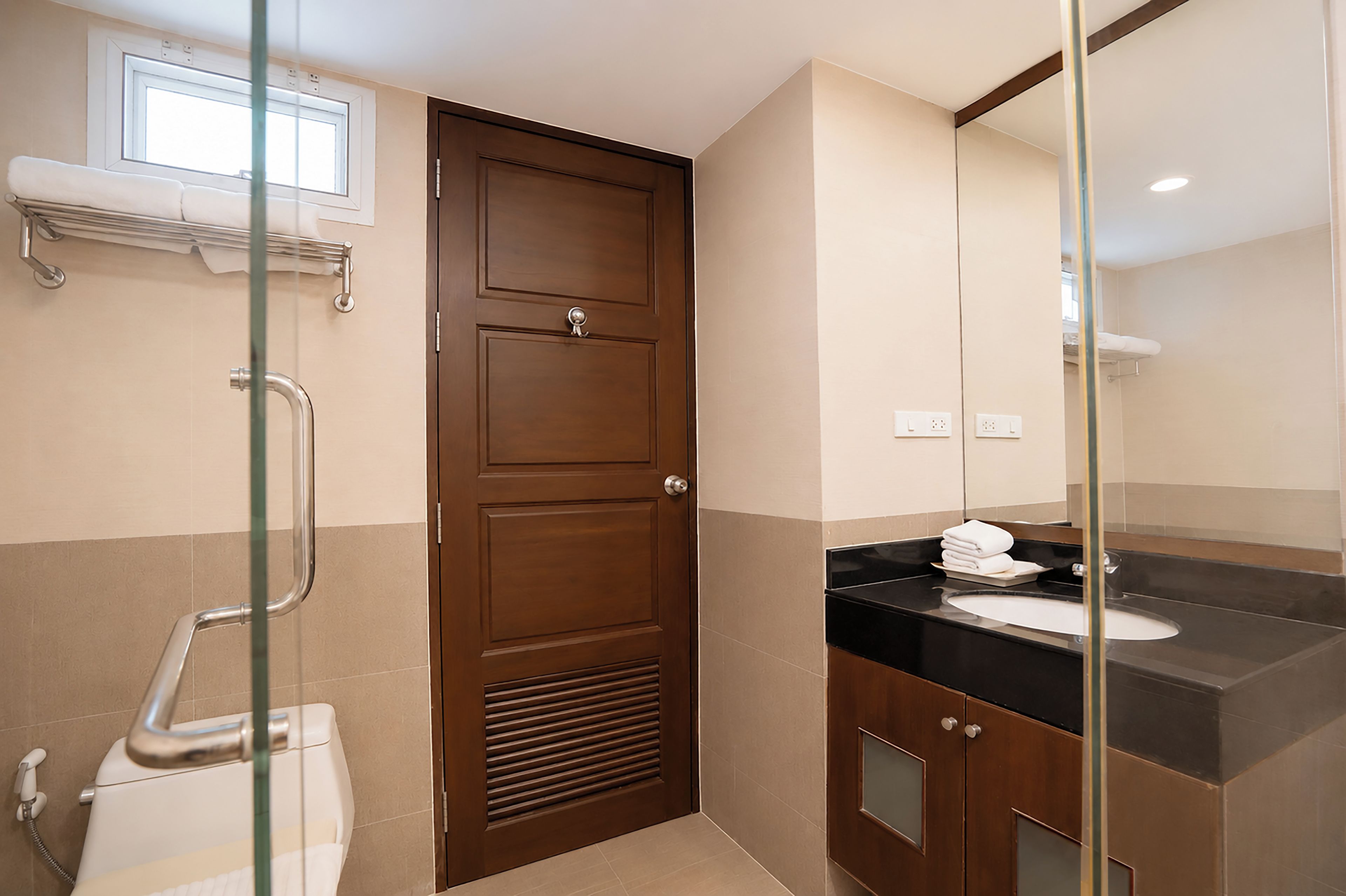 A bathroom with a wooden door, a glass shower enclosure, a white toilet, a black sink, and a mirror.