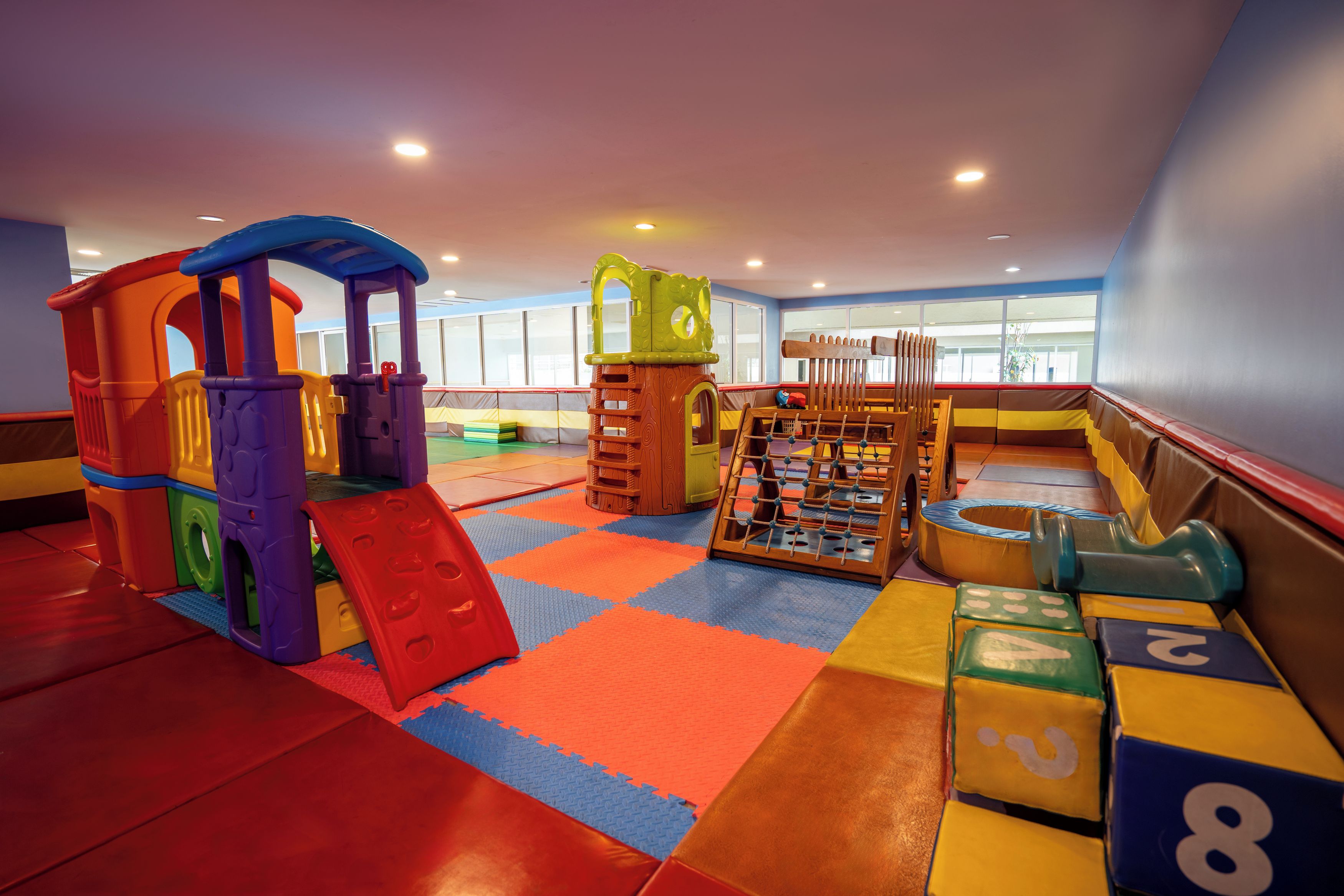 A children's play area with various play structures, a foosball table, and a seating area with cushions.