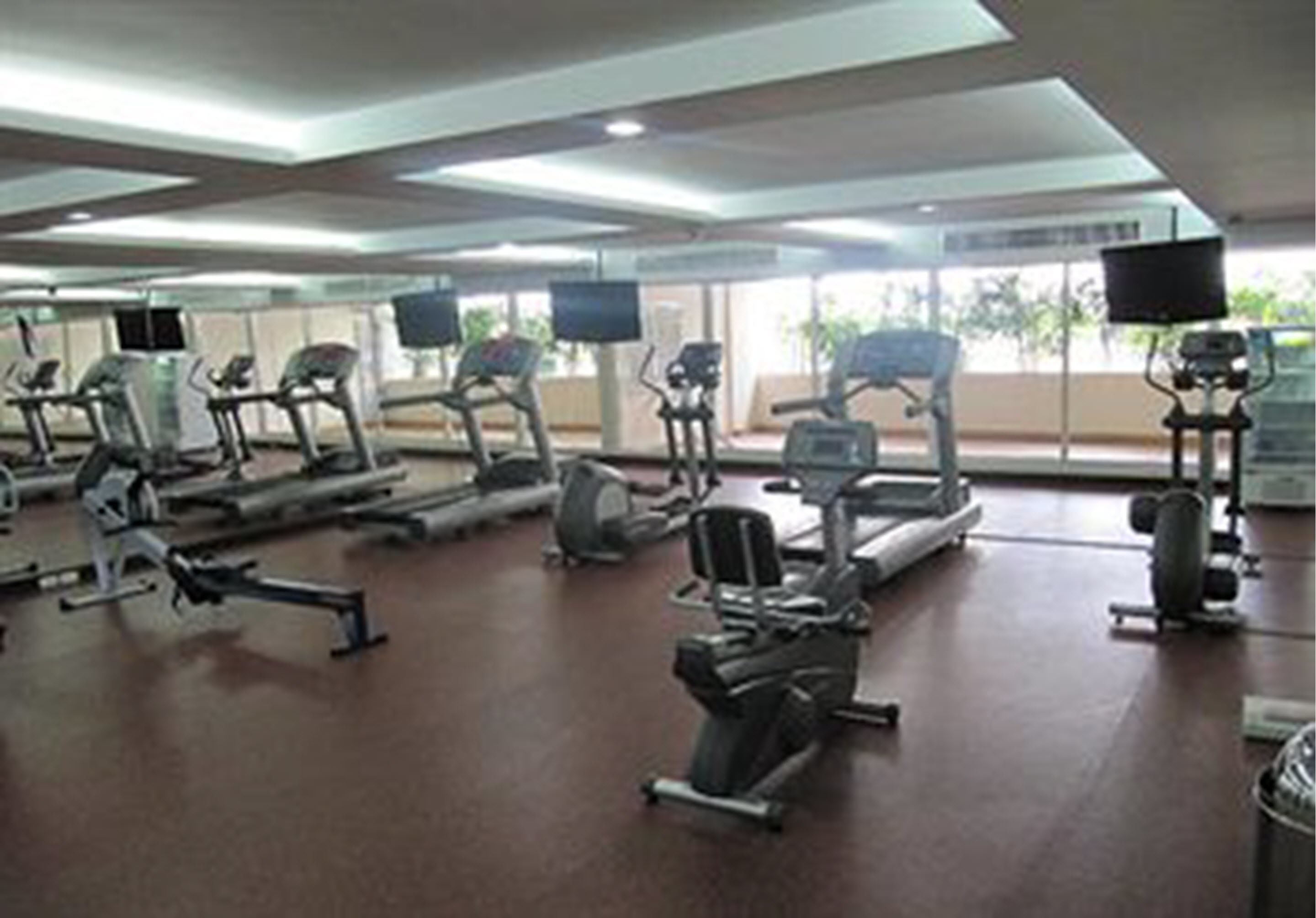 A gym with various exercise machines, large windows, and a flat-screen TV.