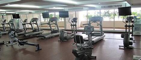 A gym with various exercise machines, large windows, and a flat-screen TV.