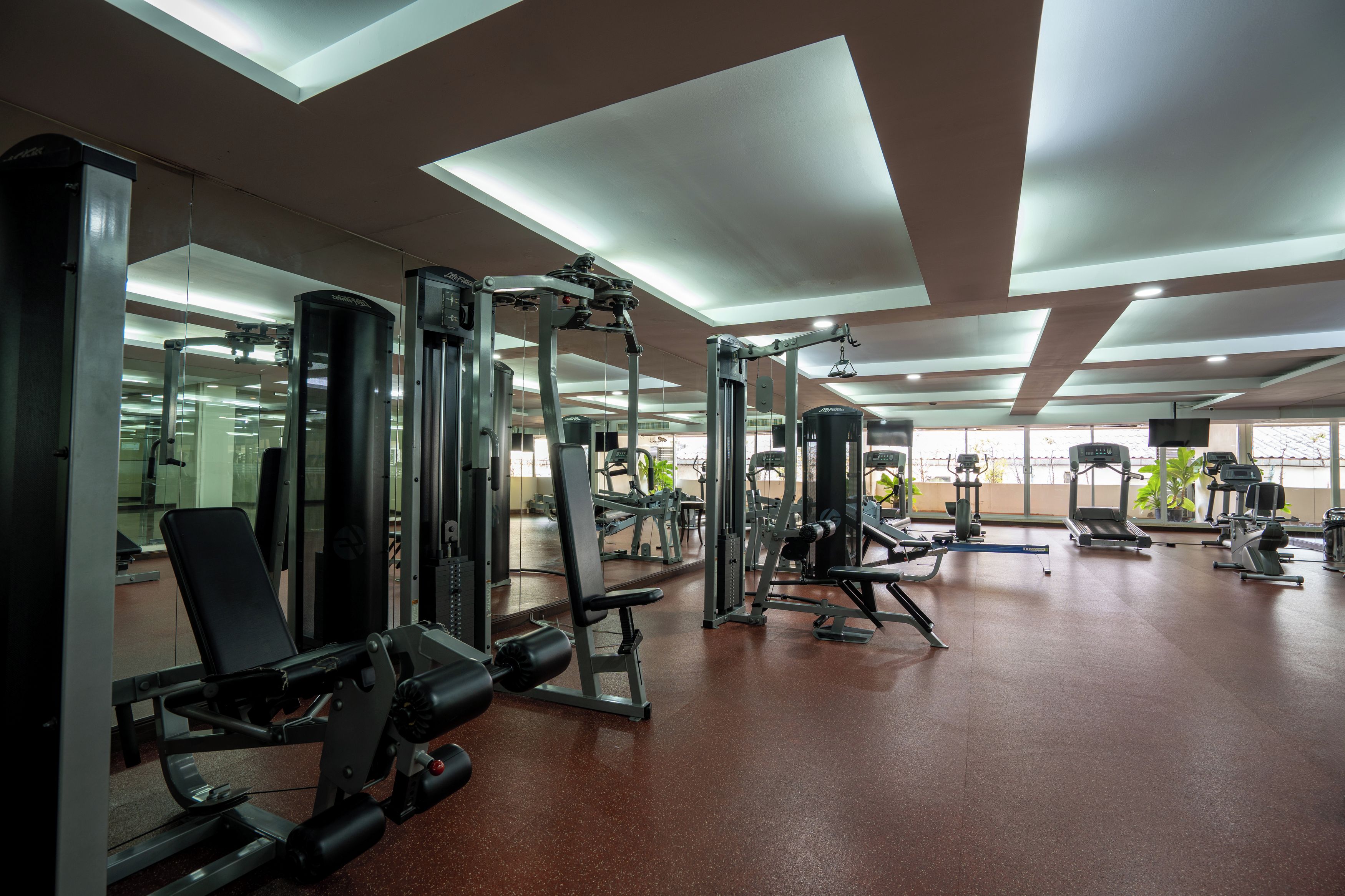 A gym with various exercise machines, mirrors, and a spacious layout.