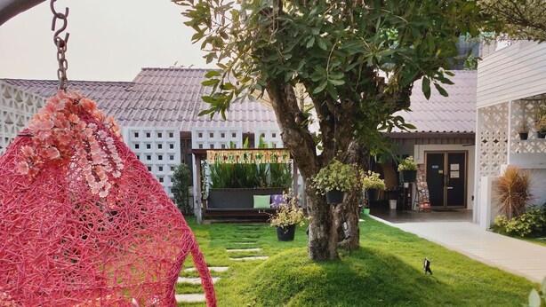A garden with a swing, a tree, and a building with a tiled roof. - Tree Residences (Chiang Mai)