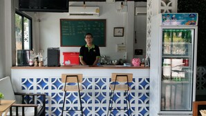 A cafe with a chalkboard menu, a refrigerator with a colorful label, and a window with a view of buildings and trees. - Tree Residences (Chiang Mai)