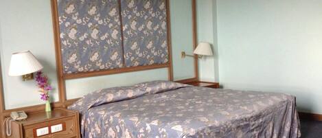 A bedroom with a bed, two bedside tables, a nightstand, a lamp, and a floral-patterned headboard.