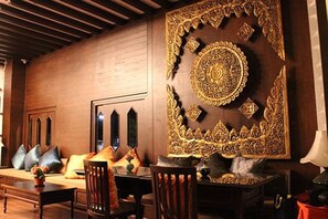 A room with a wooden wall, a large ornate tapestry, and a seating area with cushions and a table. - Baan Ratchiangsaen (Chiang Mai)