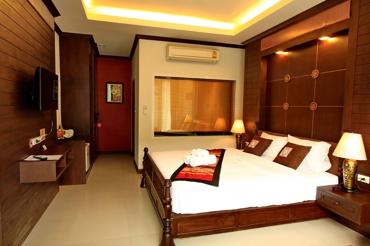 Habitación de hotel con una cama de madera, lámparas de noche, televisión de pantalla plana y una ventana con persianas.
