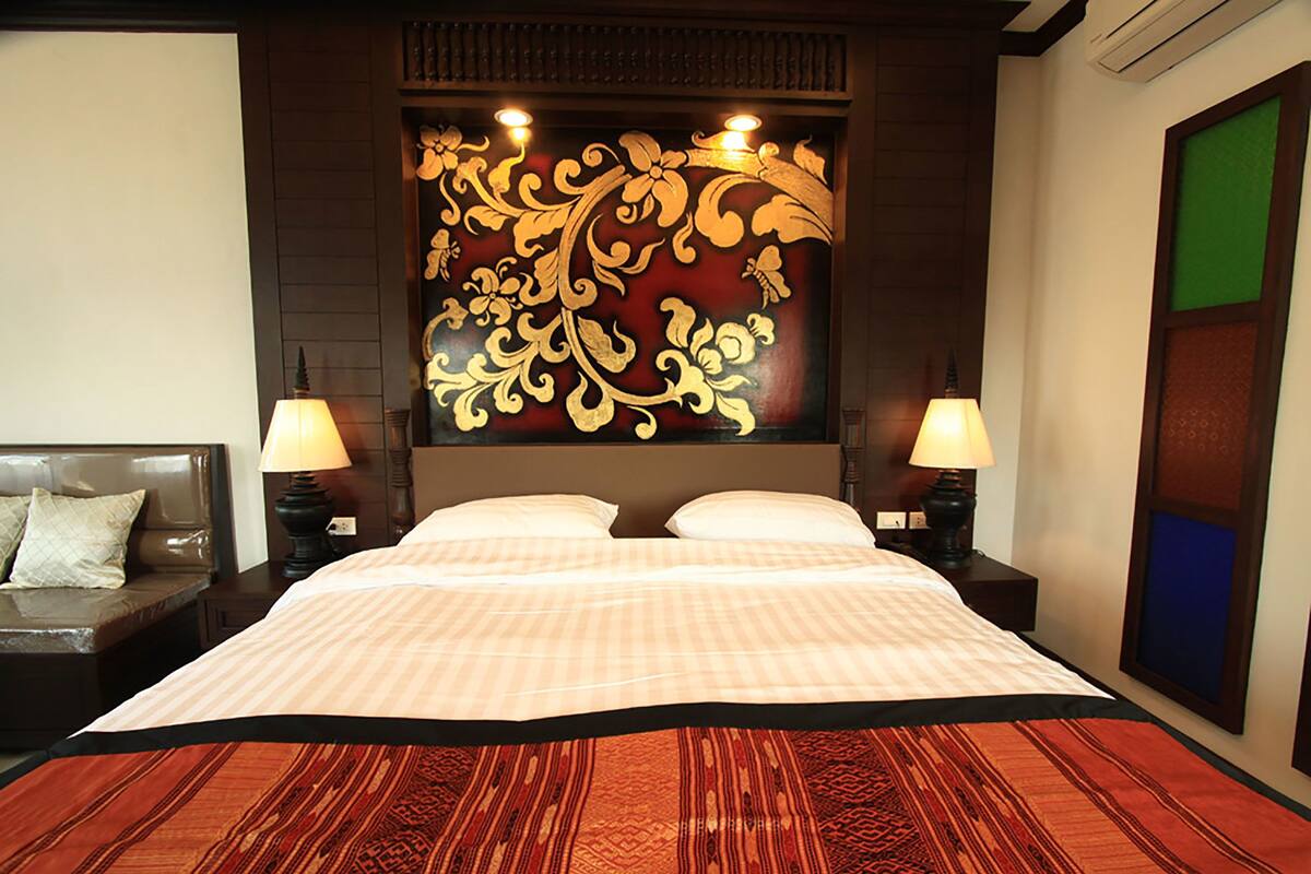 Una cama grande con una colcha estampada, dos lámparas de noche y un panel decorativo sobre la cama.