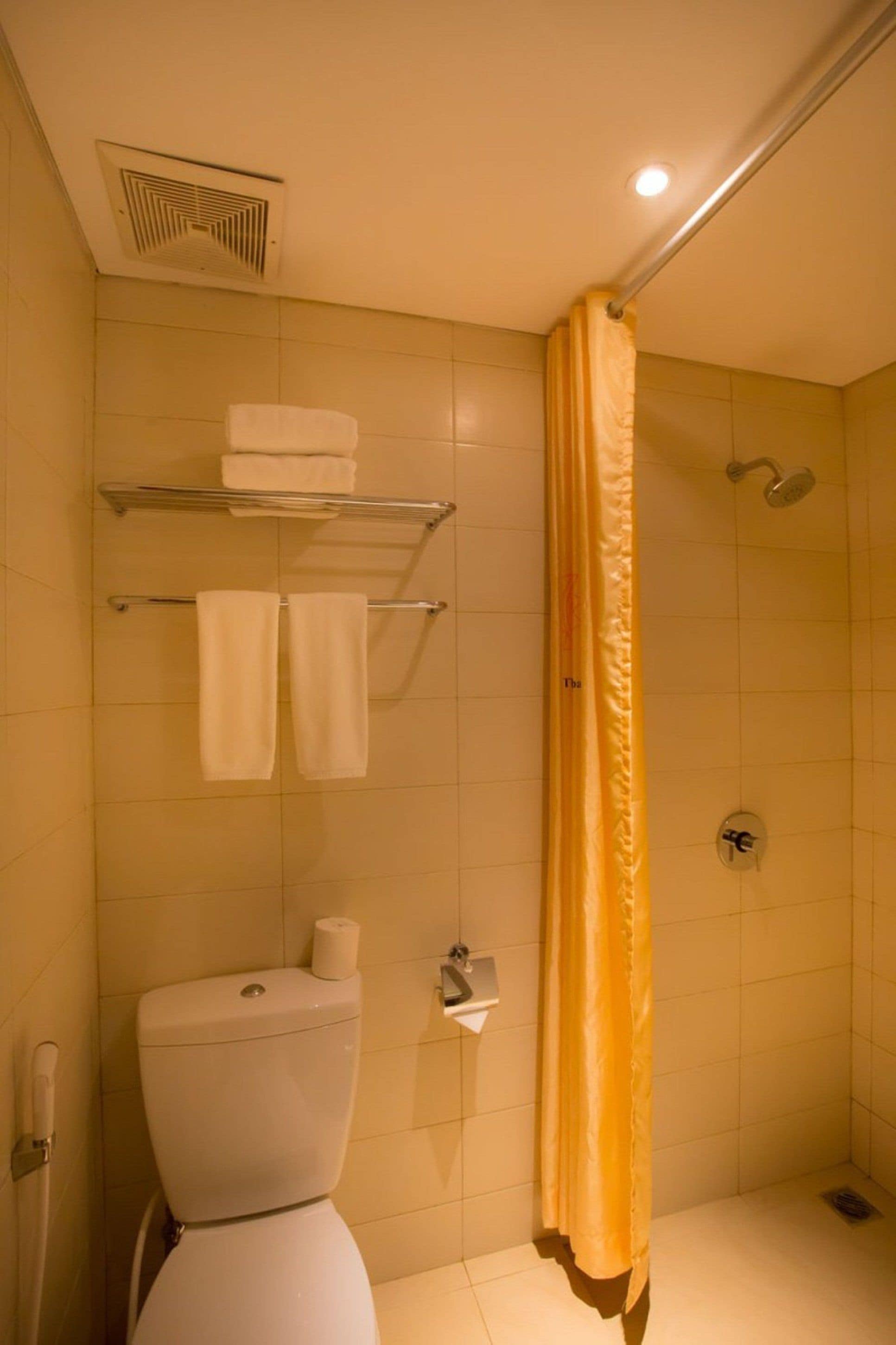 A bathroom with a toilet, a shelf with towels, a shower, and a yellow shower curtain.