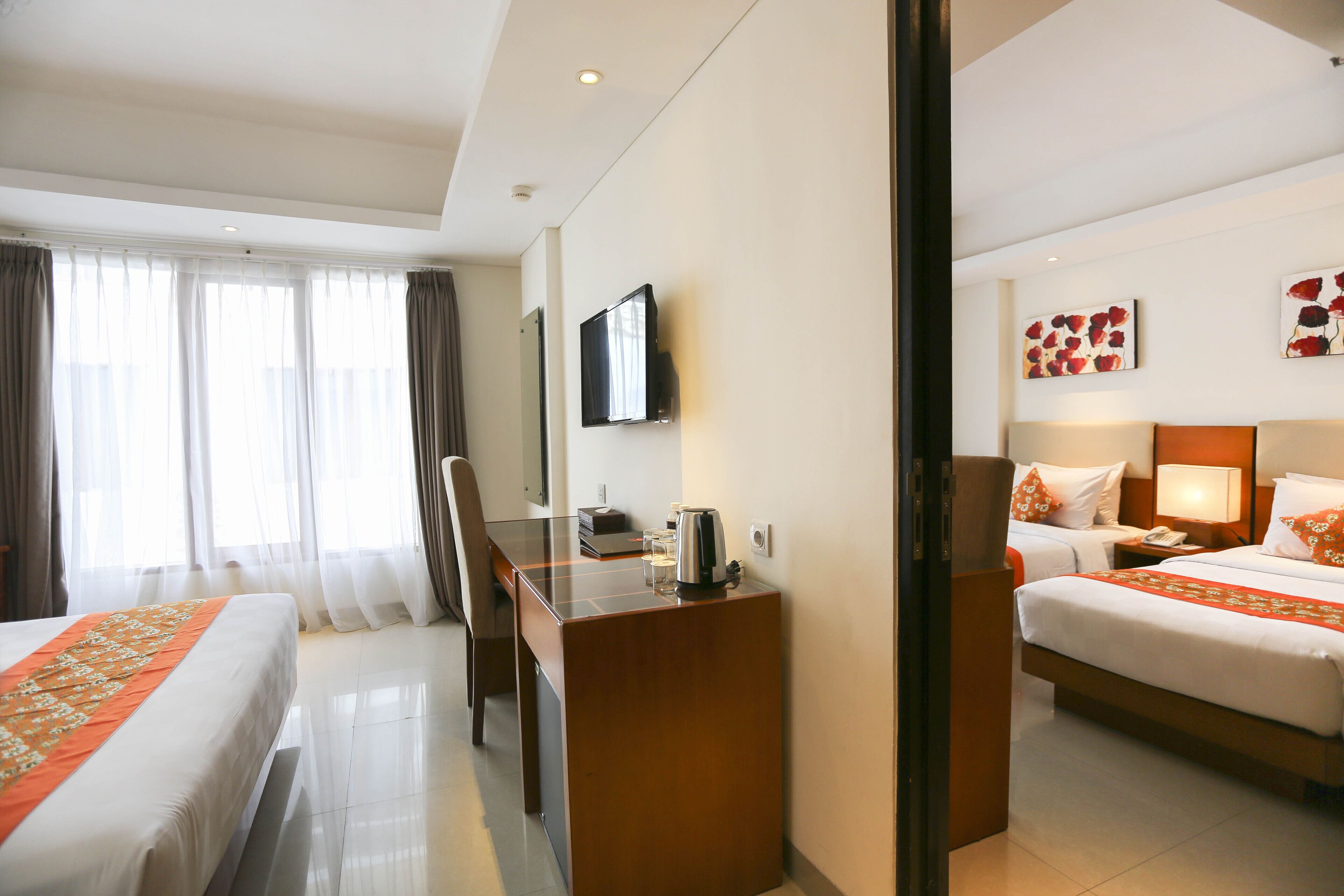 A hotel room with two beds, a desk, a chair, a television, and artwork on the walls.