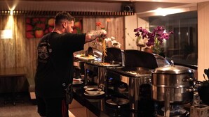 A person serving food at a buffet with various dishes and a large pot on the counter. - Bali Sun Tropical Hotel & Spa (Legian)