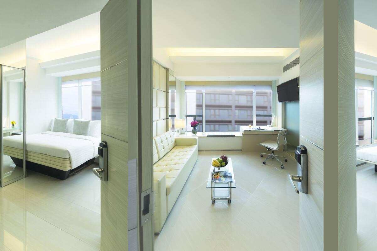 Una habitación de hotel moderna con dos camas, un escritorio, una silla y una mesita con fruta.