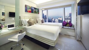 Een moderne hotelkamer met een groot bed, een bureau met een laptop, een stoel, een groot raam met uitzicht op de stad en een flatscreen-televisie.