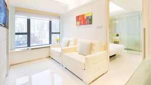 Een moderne hotelkamer met een witte bank, een schilderij aan de muur en een groot raam met uitzicht op de stad.