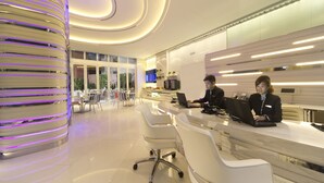 Een moderne hotellobby met een receptiebalie, een zithoek en een opvallende, cilindrische lamp.