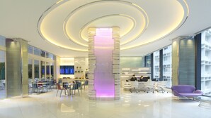 Een moderne lobby met een centrale trap, zithoeken en een receptiebalie.