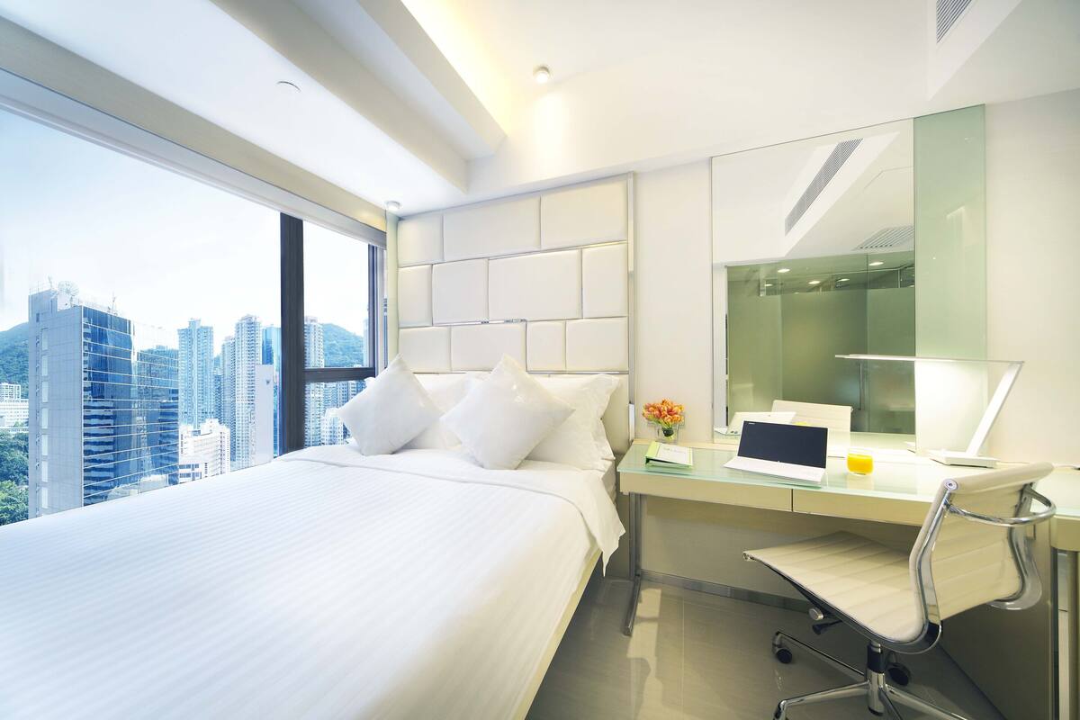 Una habitación de hotel con una cama grande, un escritorio con una computadora portátil, una silla y vistas a la ciudad.