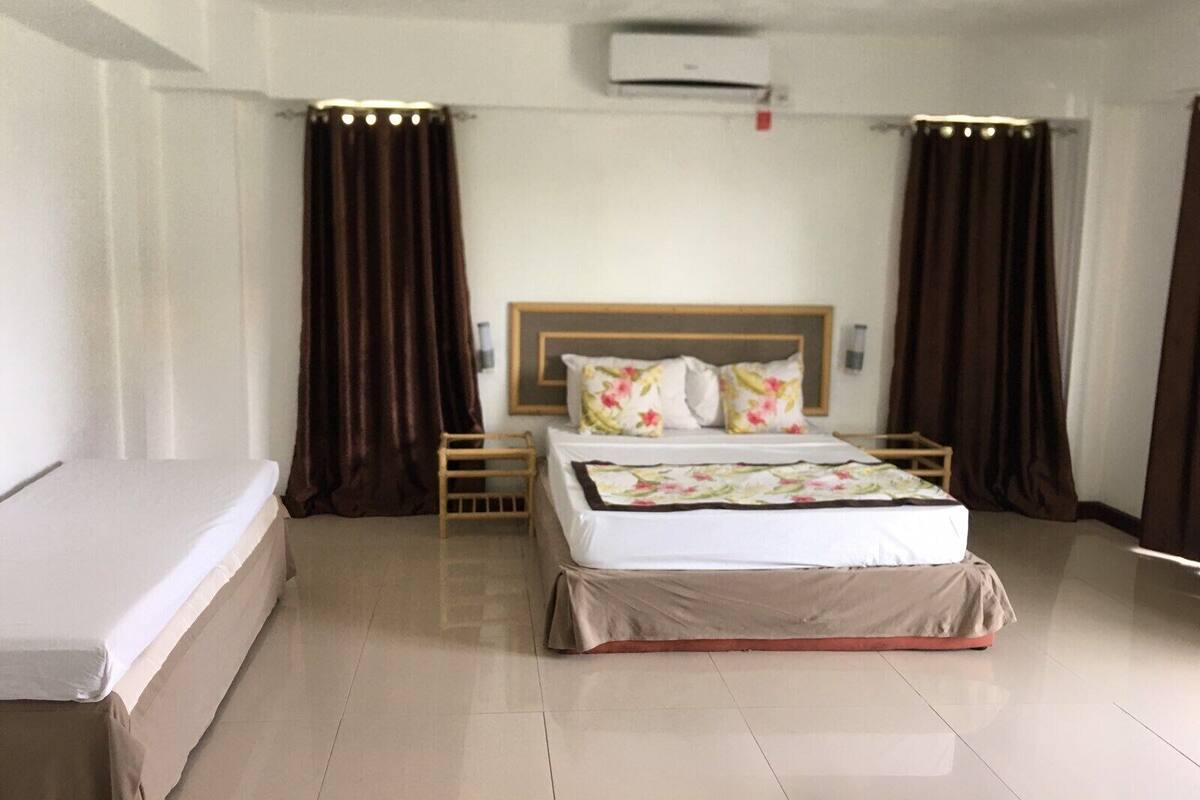 Una habitación de hotel con cama, mesita de noche, aire acondicionado y cortinas.