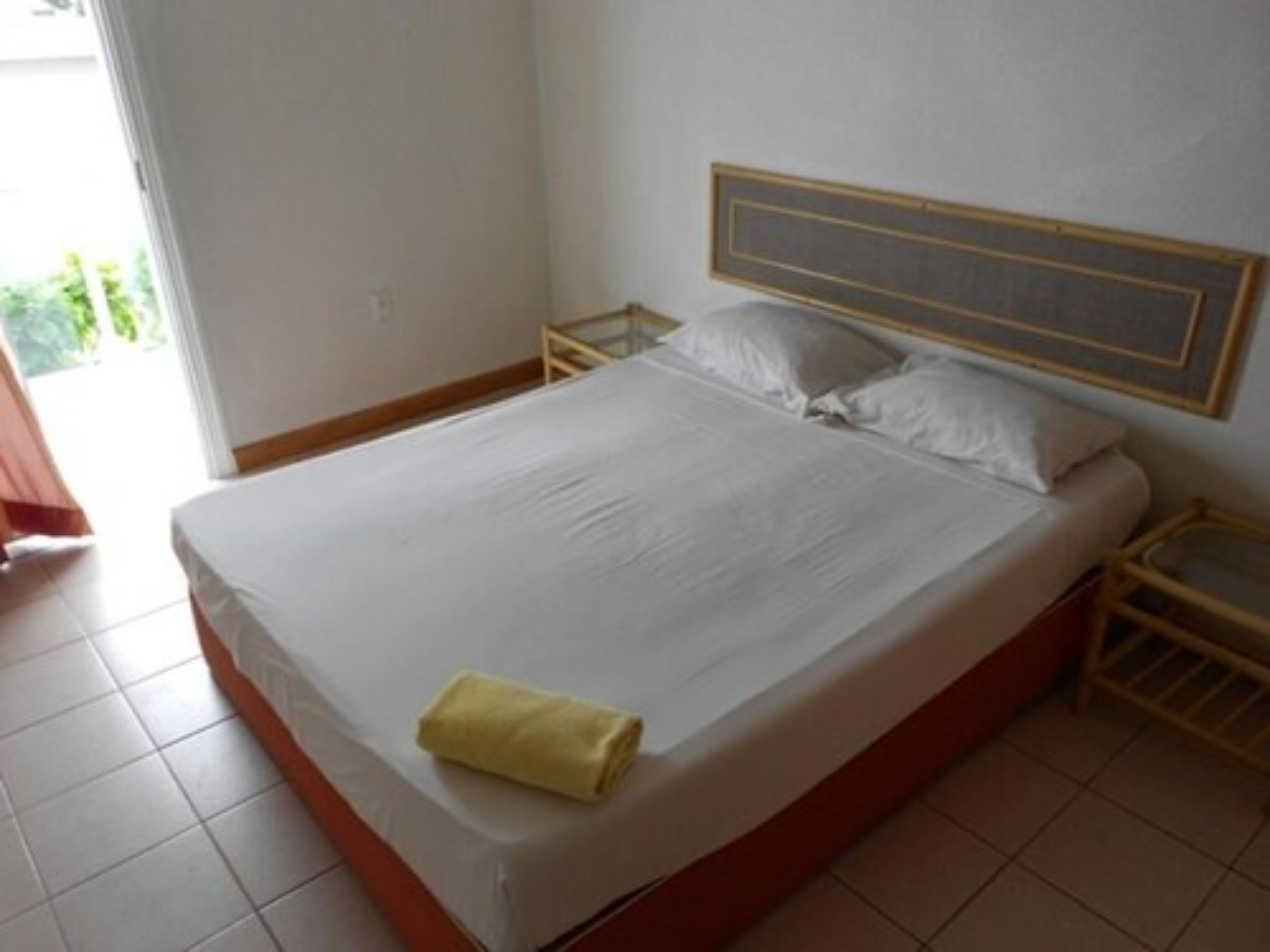 Una cama individual con cabecera de madera, una toalla amarilla y una mesita de noche con lámpara.
