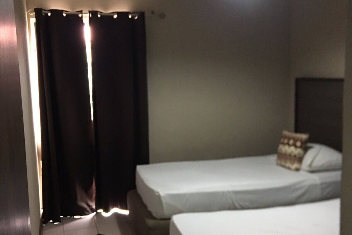 Una habitación de hotel pequeña con dos camas individuales, un ventilador de techo y piso de baldosas.