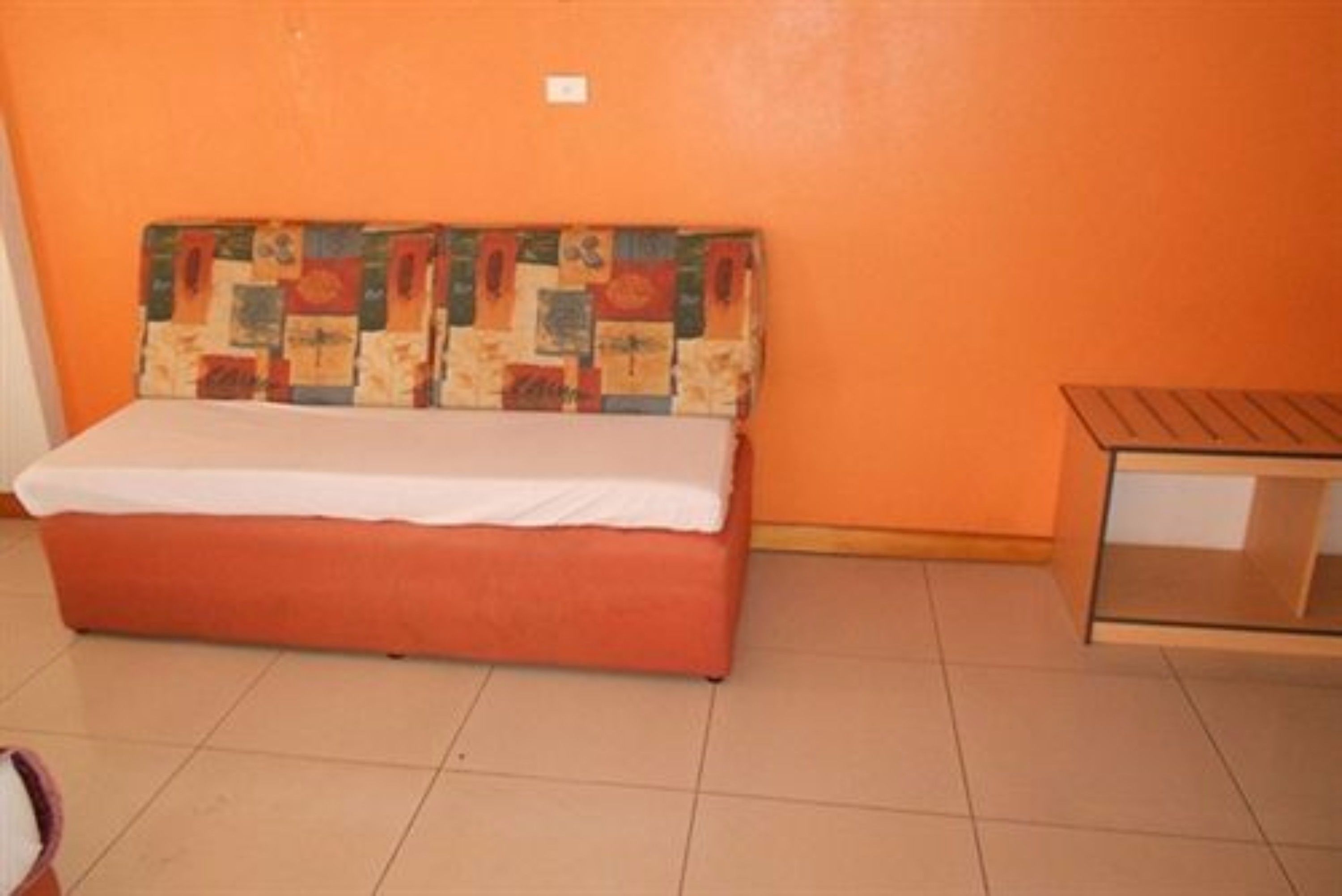 Una habitación pequeña con una cama individual, una mesita de noche de madera y un cabecero colorido en la pared.