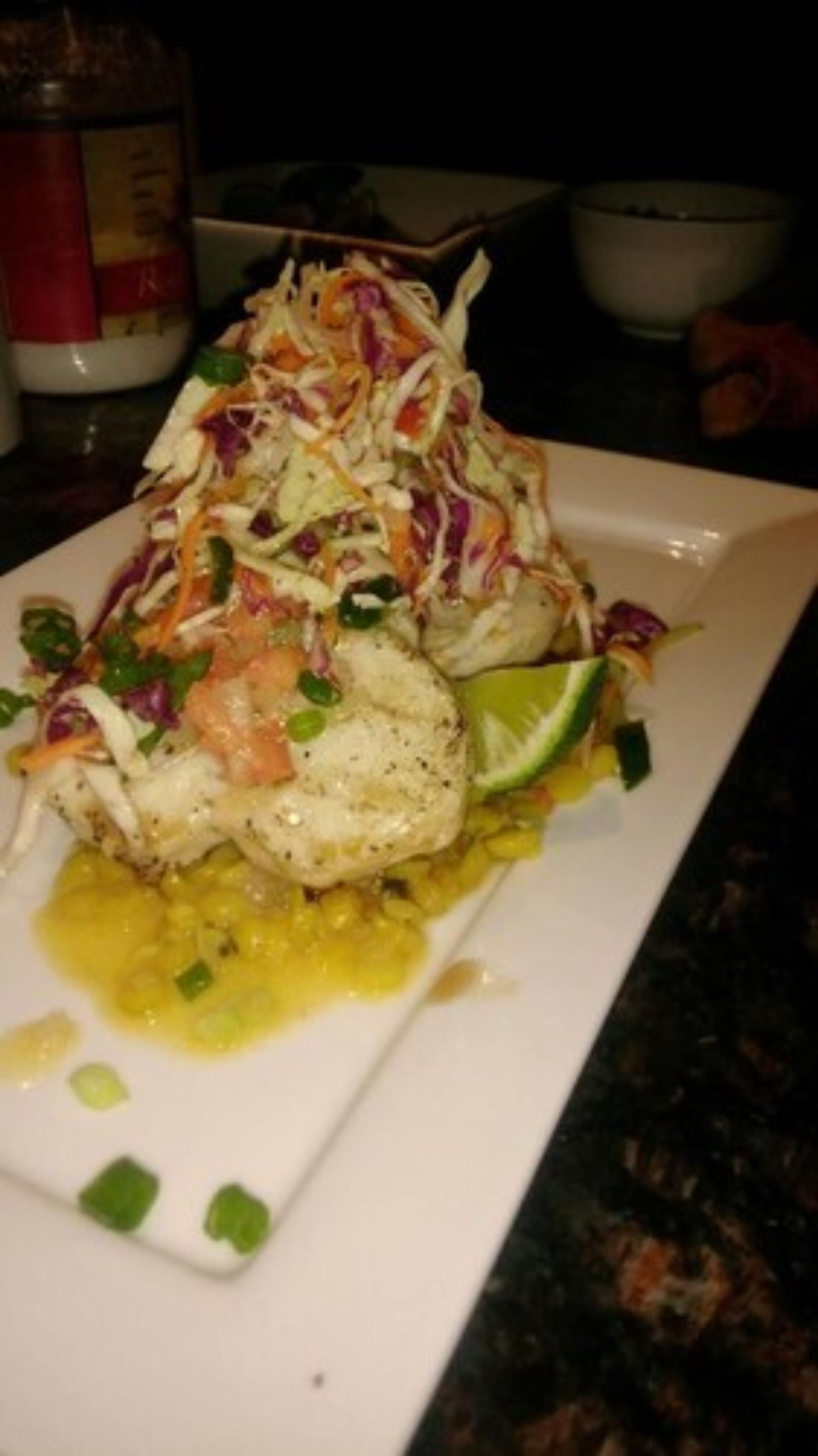Un plato de comida con un filete de pescado, ensalada de col y una cuña de lima.
