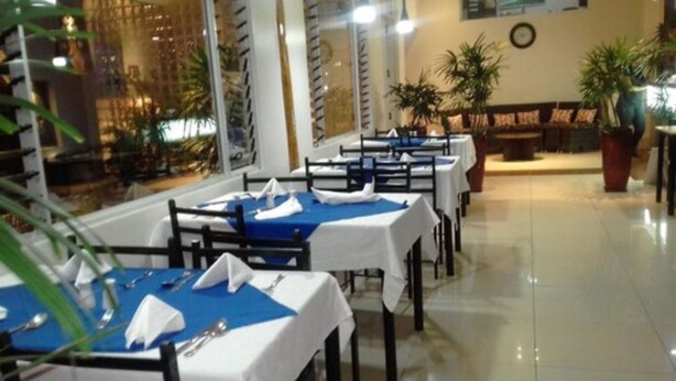 Een restaurant met gedekte tafels, een klok aan de muur en planten in potten.