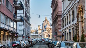 Eine Straße mit geparkten Autos und Motorrädern, die zu einem Gebäude mit einer Kuppel und einem Glockenturm führt.