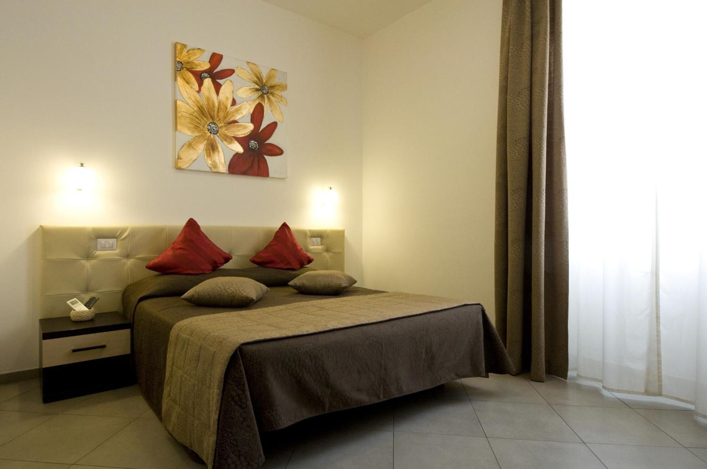 A bedroom with a bed, nightstands, a lamp, and a floral painting on the wall.