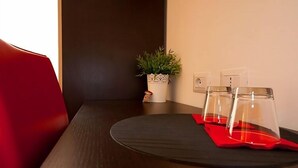 Ein Esstisch mit schwarzem Tischläufer, roten Servietten und klarem Glasgeschirr. An der Wand neben dem Tisch steht ein Topfpflanze.