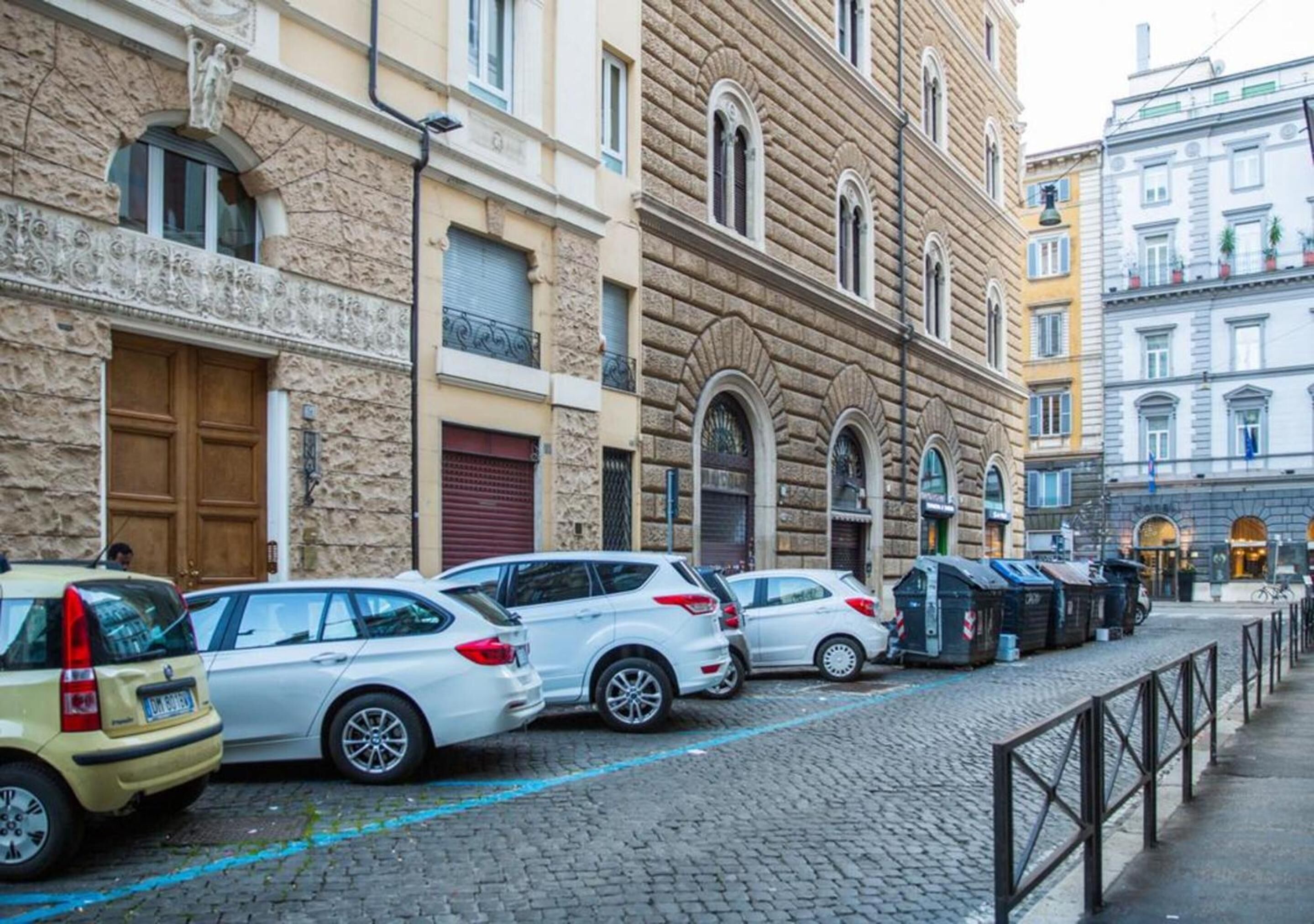Eine Kopfsteinpflasterstraße gesäumt von parkenden Autos und historischen Gebäuden mit Rundbogenfenstern und dekorativem Steinwerk.