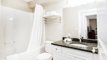 A modern bathroom with a white toilet, a shower with a white curtain, a sink with a granite countertop, and a mirror above the sink.