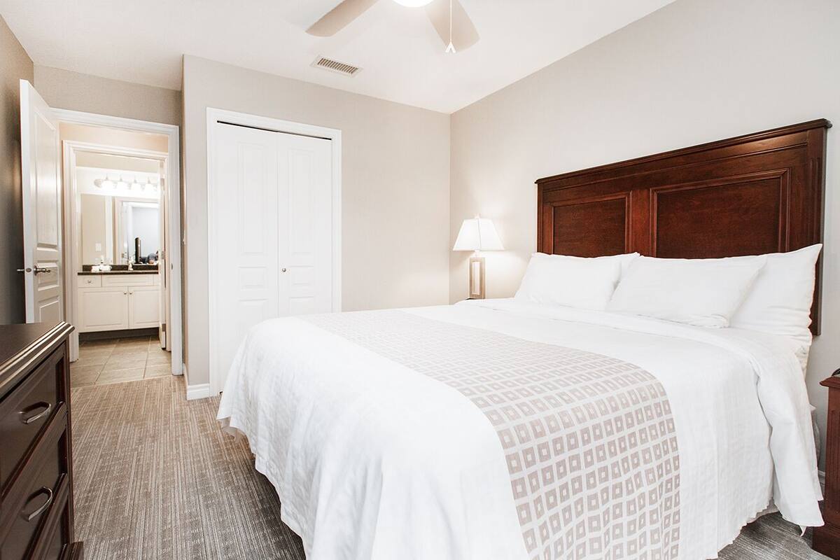 A neatly arranged bedroom with a large bed, a bedside lamp, and a wooden headboard.