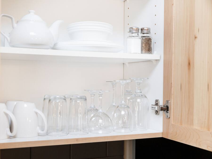 A kitchen cabinet with white dishes, a teapot, and various glassware.