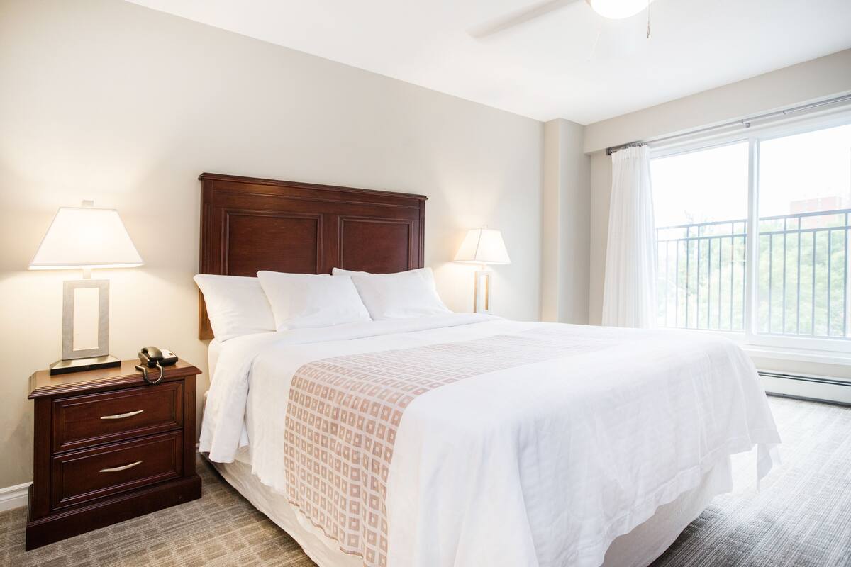 A neatly made bed with a wooden headboard, two bedside lamps, and a nightstand with drawers.