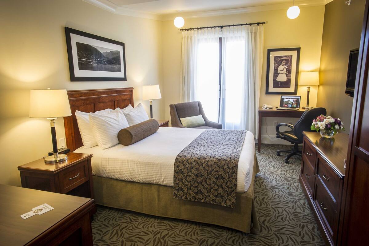 Habitación de hotel con cama, dos lámparas de noche, escritorio con una computadora portátil, una silla y un aparador.