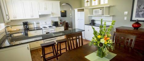 Une cuisine moderne avec des meubles blancs, un plan de travail en granit et un coin repas comprenant une table et des chaises en bois.