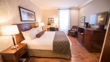A hotel room with a large bed, bedside lamps, a desk with a chair, a television, and a framed picture on the wall.