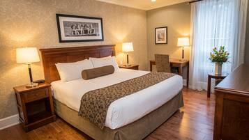 Une chambre d’hôtel avec un grand lit, deux tables de chevet avec des lampes, une chaise, un bureau et une fenêtre avec des rideaux.