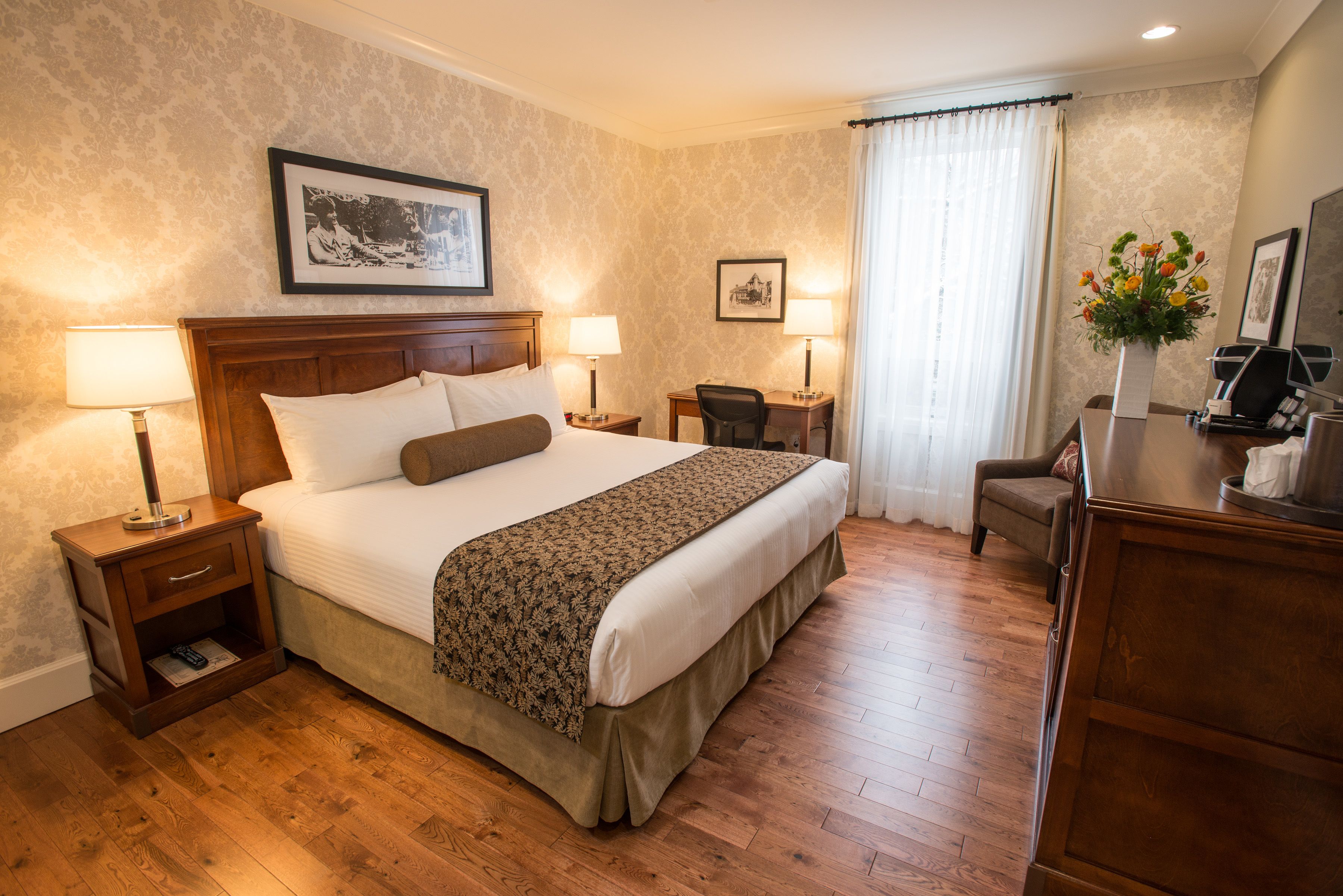 Une chambre d’hôtel avec un grand lit, deux tables de chevet avec des lampes, un bureau, une chaise et une commode.