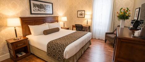 Une chambre d’hôtel avec un grand lit, deux tables de chevet avec des lampes, un bureau, une chaise et une commode.
