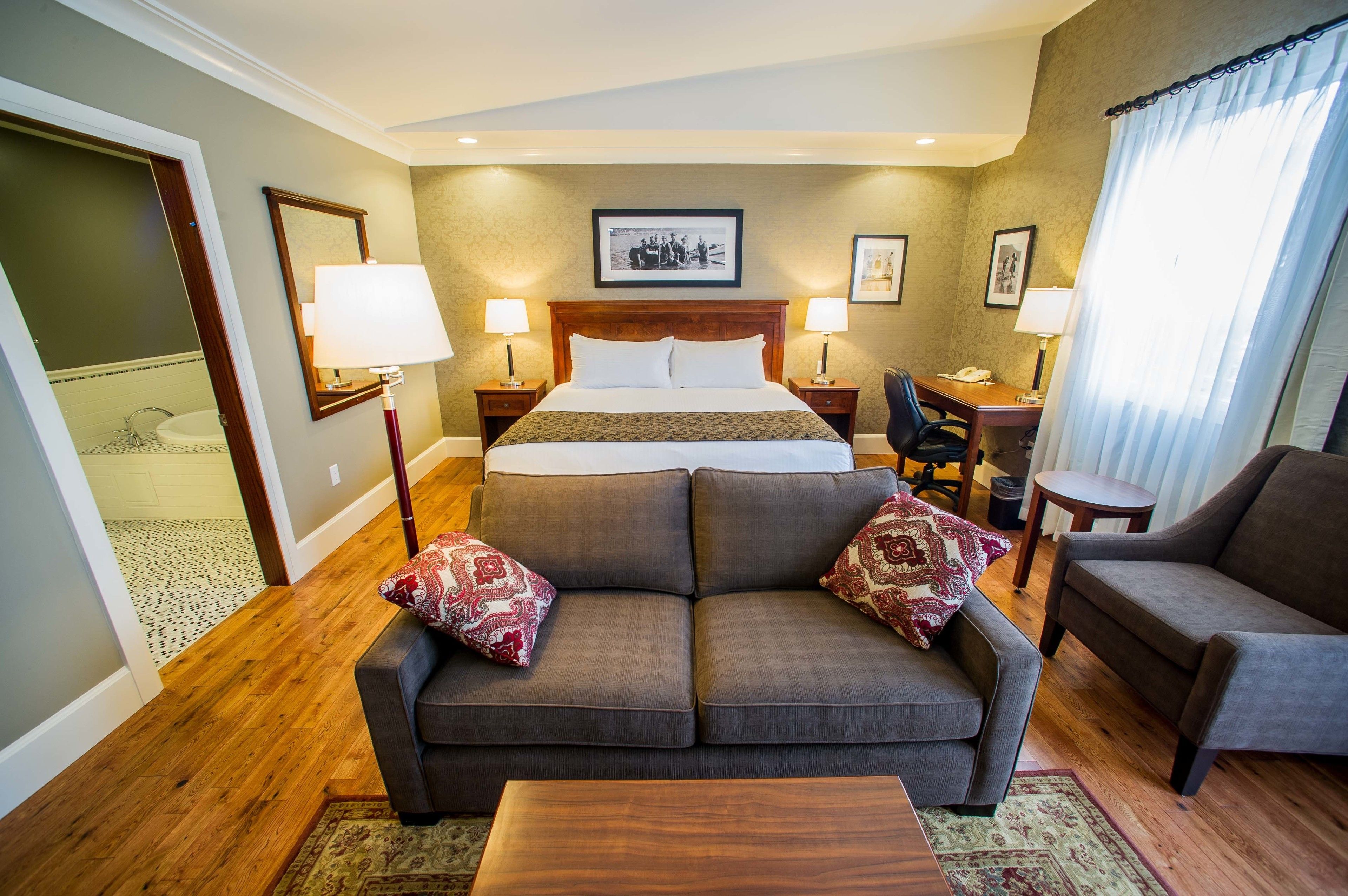 Une chambre d’hôtel avec un grand lit, deux tables de chevet avec des lampes, un canapé, un fauteuil et un bureau.