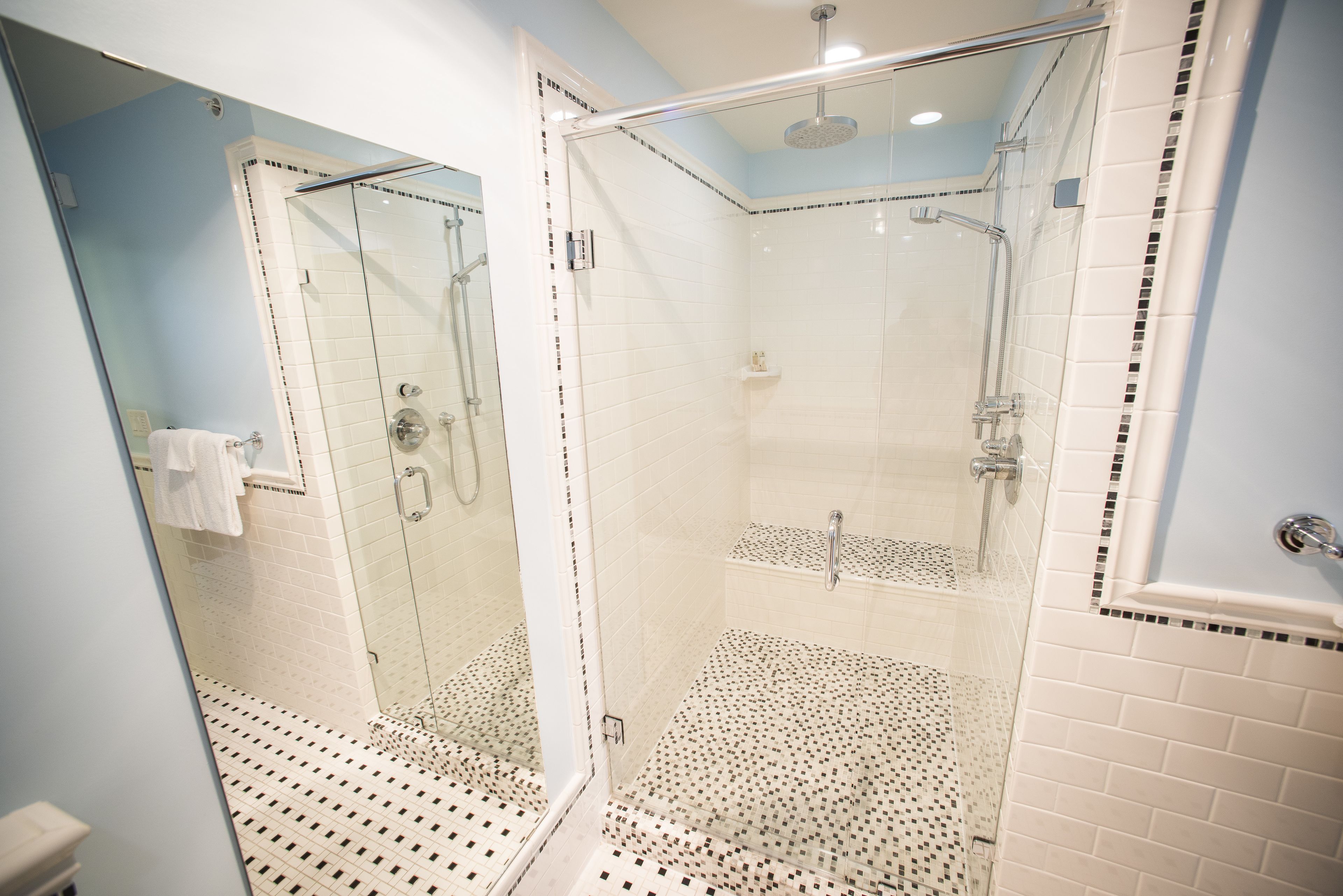 A modern bathroom with a glass-enclosed shower, white tiled walls, and a patterned floor.