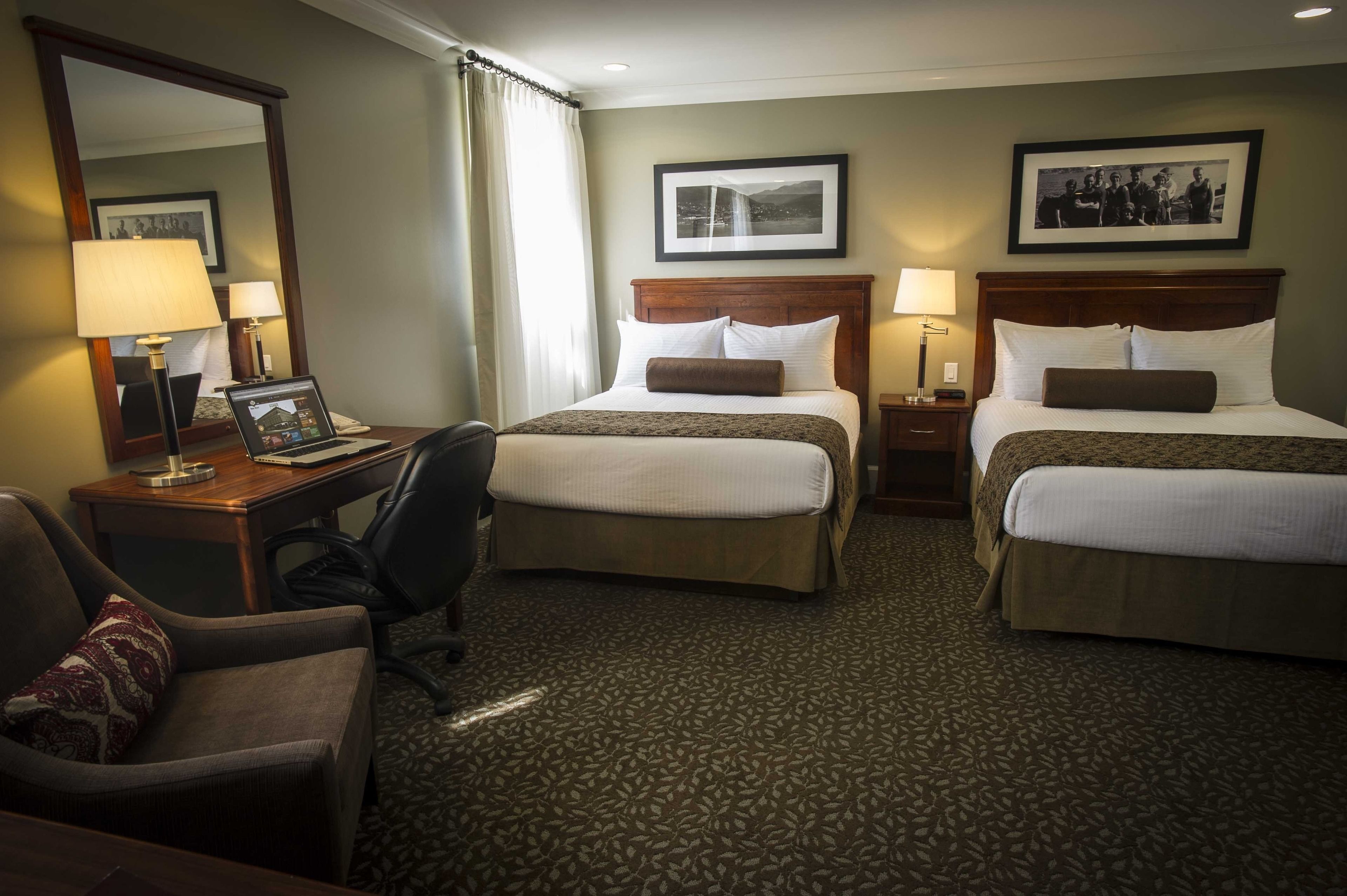 A hotel room with two beds, a desk with a laptop, a chair, and a large mirror.