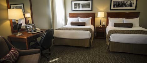 A hotel room with two beds, a desk with a laptop, a chair, and a large mirror.