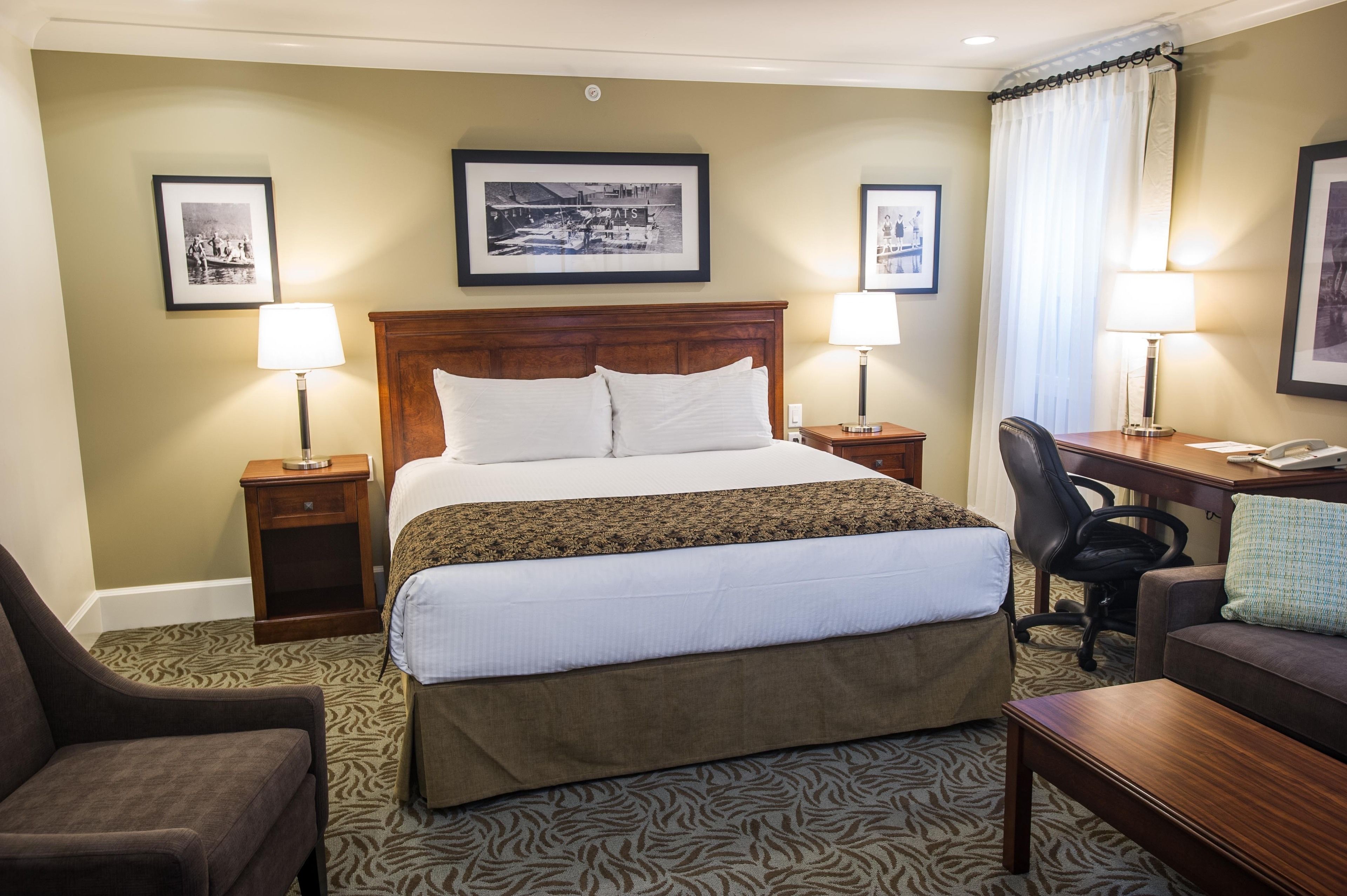 A hotel room with a large bed, two bedside tables with lamps, a desk with a chair, and a couch.